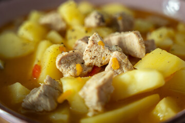 A bowl of soup with meat and potatoes. The meat is cut into small pieces and the potatoes are cooked. The soup is orange and has a spicy flavor
