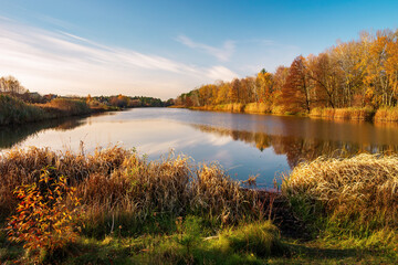 A tranquil autumn scene featuring a calm lake surrounded by vibrant fall foliage. Golden hour light...