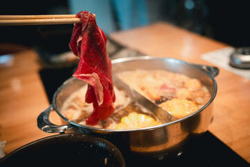 Chopsticks picking up succulent slices of beef to boil in hot pot, showcasing the deliciousness and freshness of the ingredients.