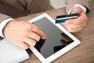 Man with credit card using tablet at wooden table, closeup