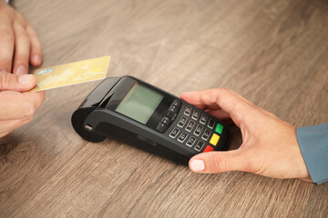 Woman taking payment from client via credit card terminal at wooden table, closeup