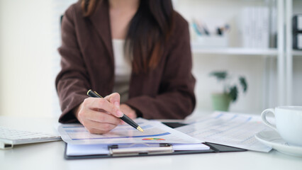 Professional businesswoman working at her desk, reviewing financial documents while using a laptop.