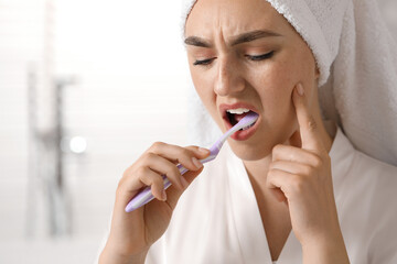 Young woman suffering from toothache while brushing her teeth in bathroom