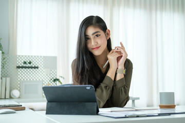 Confident young woman with long dark hair is seated at a sleek, modern desk, holding a stylus in...