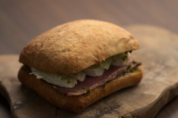 Roast beef and mozzarella sandwich with ciabatta bun on olive board
