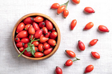 Fresh rose hips in a wooden bowl on linen. Also rose haw or rose hep, intense red ripe fruits, used for herbal teas, jam and can be eaten raw. One of the richest vitamin C sources available in plants.