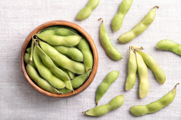 Fresh edamame, green soybeans in the pod, in a wooden bowl, on linen. Raw immature soybeans, Glycine max, used boiled or steamed and salted, as a common side dish and appetizer in Japanese cuisine.