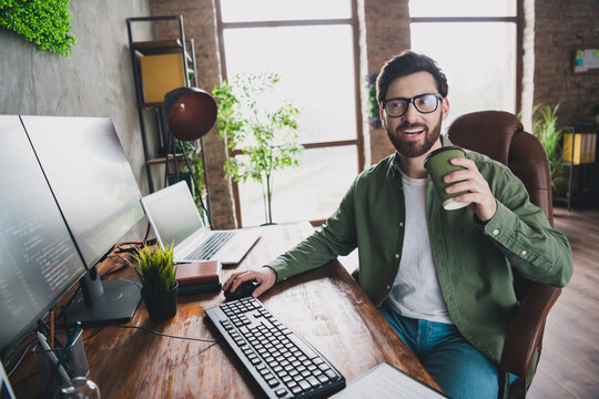 Photo of professional it specialist young man sit chair drink coffee computer desktop loft interior office indoors