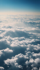 Aerial view of fluffy white clouds against a blue sky, with distant mountain silhouettes visible through the clouds. The scene captures a serene and tranquil atmosphere.