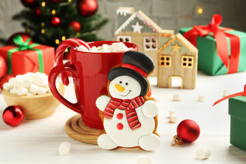 Delicious cookie in shape of snowman, cup with cocoa and Christmas decor on white wooden table