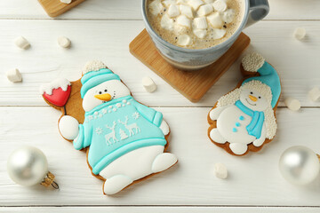 Delicious cookies in shape of snowmen, cup with cocoa and Christmas decor on white wooden table, flat lay