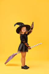Obraz premium Cute girl with broom dressed like witch on yellow background. Halloween celebration