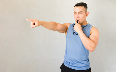 Dedicated male personal trainer using a whistle and giving instructions during a workout session