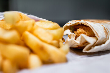 Crispy fries and pita bread with chicken, lettuce, tomato and sauce. Close-up of fries with blurring effect