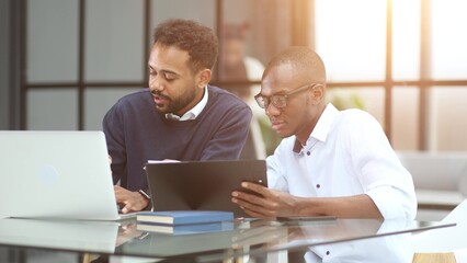 Smiling group of diverse businesspeople going over paperwork together and working on a laptop