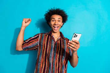 Portrait of nice young man raise fist hold phone wear shirt isolated on turquoise color background