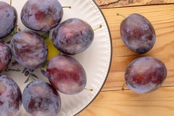 Ripe plums in a ceramic dish on a wooden table, macro, top view.