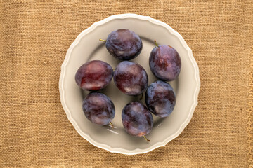 Sweet plums in a ceramic plate on a jute cloth, macro, top view.