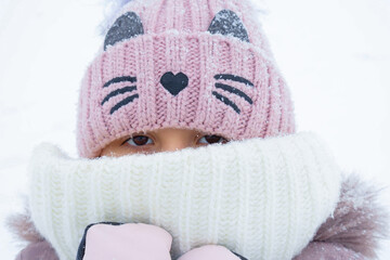 Child bundled in winter attire with a pink knitted hat and scarf enjoying snowy weather outdoors
