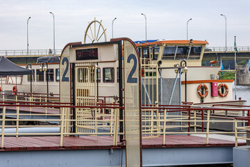 Bridge at entrance number 2 of embankment in small tourist boat harbour, boat anchored at the quay, bridge in background, cloudy day in Maastricht, South Limburg, Netherlands