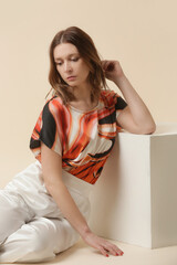 Female model wearing silk outfit,  marble orange camisole top and white trousers. Classic and...