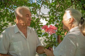 Happy active senior husband gives flowers to his wife. Lifestyle of couple in retirement. Elderly woman and retired man having fun together outdoors in summer.