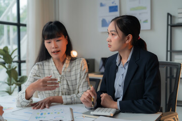 Two businesswomen are having a discussion about financial data while sitting at a table in the office. They're working together to analyze charts and graphs