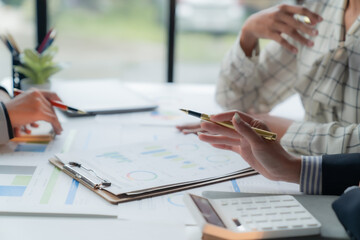 Team of business professionals gathered around a table, reviewing financial reports and using a calculator, engaged in a collaborative effort to analyze data and plan their business strategy