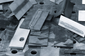 A pile of metal pieces with a few of them having holes in them. The pile is on a table. metalworking concept background