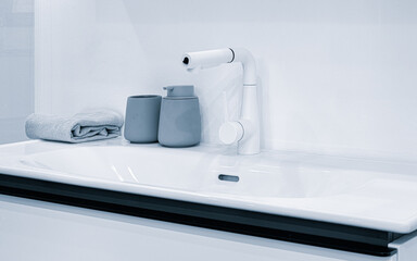 Fototapeta premium A white sink with a silver faucet and a soap dispenser. A towel is on the counter next to the sink