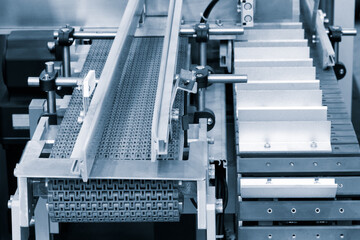 A conveyor belt with a white and silver color is moving. The conveyor belt is made of metal and has a silver color. It is moving at a steady pace and is transporting items from one place to another