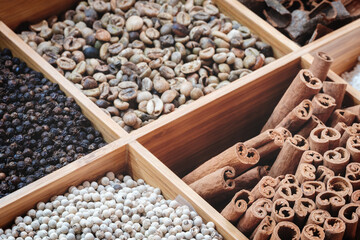 A wooden box with a variety of spices and nuts. The spices include cumin, cinnamon, and pepper