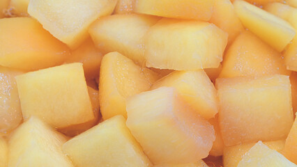 A close up of a pile of yellow fruit cubes. The fruit cubes are frozen and appear to be cut into small pieces. Concept of abundance and freshness, as the fruit cubes are piled high