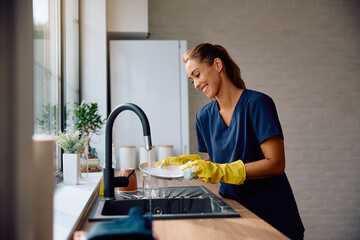 Happy woman washing dishes in kitchen.