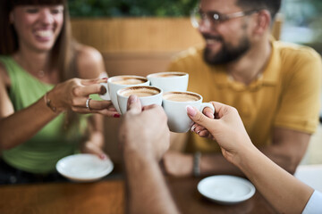 Close-up of  a group of friends toasting with cups of coffee at a cafe. Focus is on cups of coffee 
