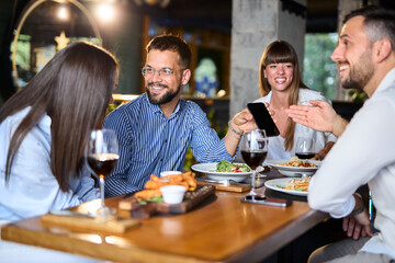Group of happy business colleagues using cell phone during lunch in a restaurant