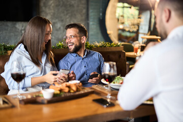 Group of happy business colleagues using cell phone during lunch in a restaurant