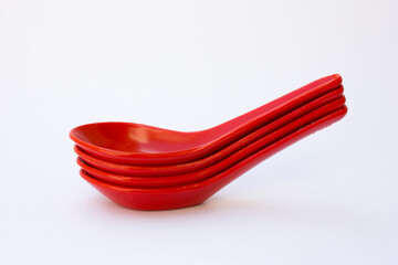 A stack of red chinese spoon. It features a short, thick handle that extends directly from a deep, flat bowl, making it particularly well-suited for serving and consuming liquids, such as soups, or l