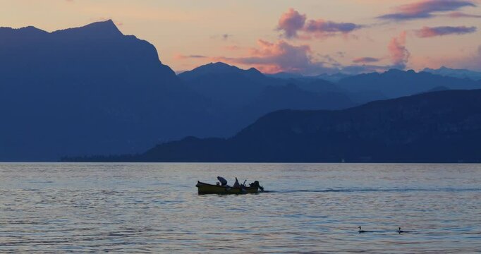 A boat with a fisherman floating on the Lake Garda at sunset, view from Lazise town shore, Italy, Europe.