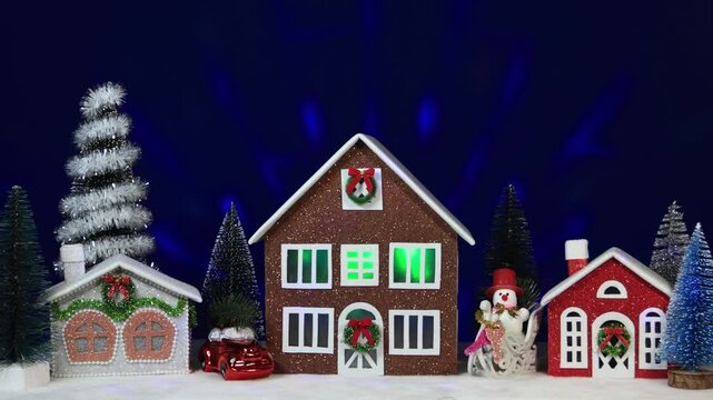 Three colorful Christmas houses surrounded by a Christmas tree, a car and a snowman on a sled
