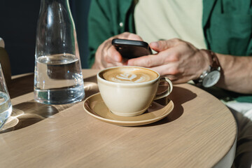 Close-up of a cup of coffee on the table against the background of a man using his mobile phone