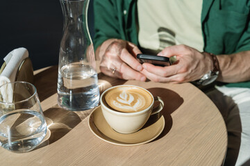 Close-up of a cup of coffee on the table against the background of a man using his mobile phone