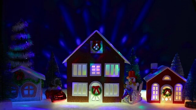 A town of Christmas houses surrounded by a Christmas tree, a car and a snowman on a sled