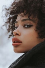 A woman with curly hair and a red lipstick is standing in front of a white background. Concept of confidence and boldness, as the woman's makeup and hairstyle are both striking and attention-grabbing