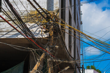 A chaotic jumble of exposed electrical and communication wires hang dangerously from a crumbling building in a busy urban area of Delhi, India