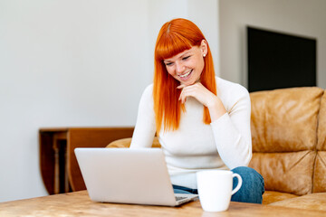 Young Woman With Vibrant Orange Hair Enjoys Cozy Moment Working on Her Laptop at Home