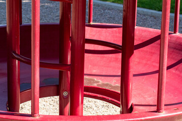 Closeup view of inside of circular red playground climbing structure on sunny day with dramatic shadows