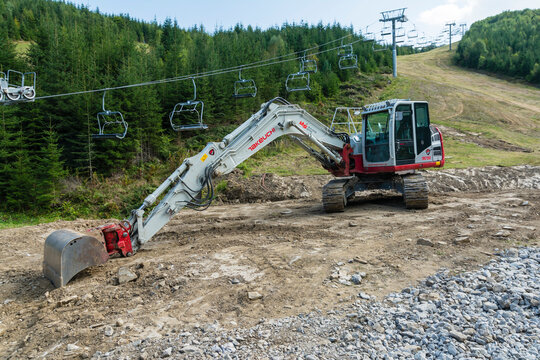 Takeuchi tb2150 crawler excavator with bucket on a construction site next to a ski slope in the mountains.