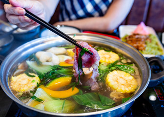 Chopsticks picking up beef in a boiling shabu with a woman's hand in the blurred background