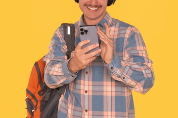 Smiling Man With Headphones and Backpack Checks Smartphone Against Bright Yellow Background